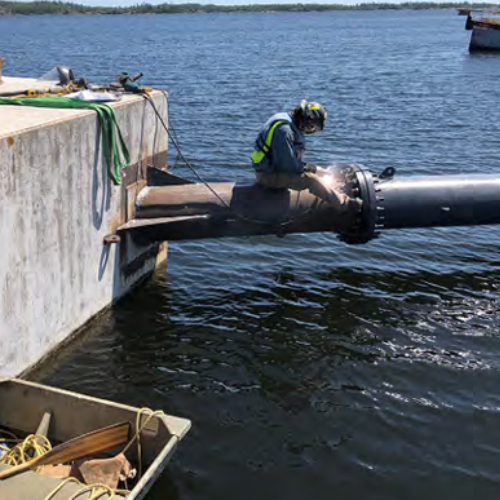 A welder working on a pipeline over a lake.